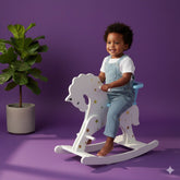 Child sitting on a white rocking horse with star patterns against a purple background
