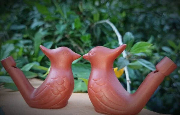 HD Two terracotta bird-shaped watering cans on a wooden surface with a green leafy background.