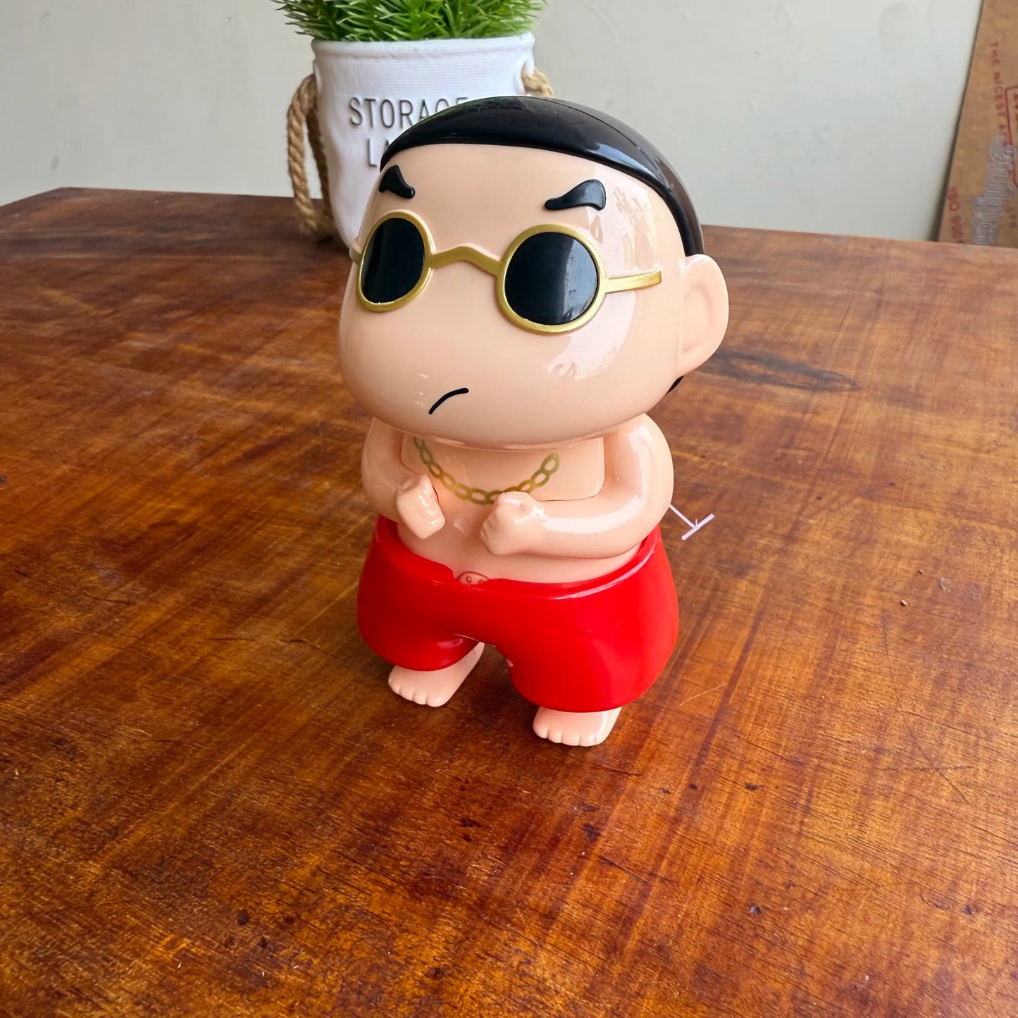 Cartoon shinchan character figurine with sunglasses and red shorts on a wooden surface